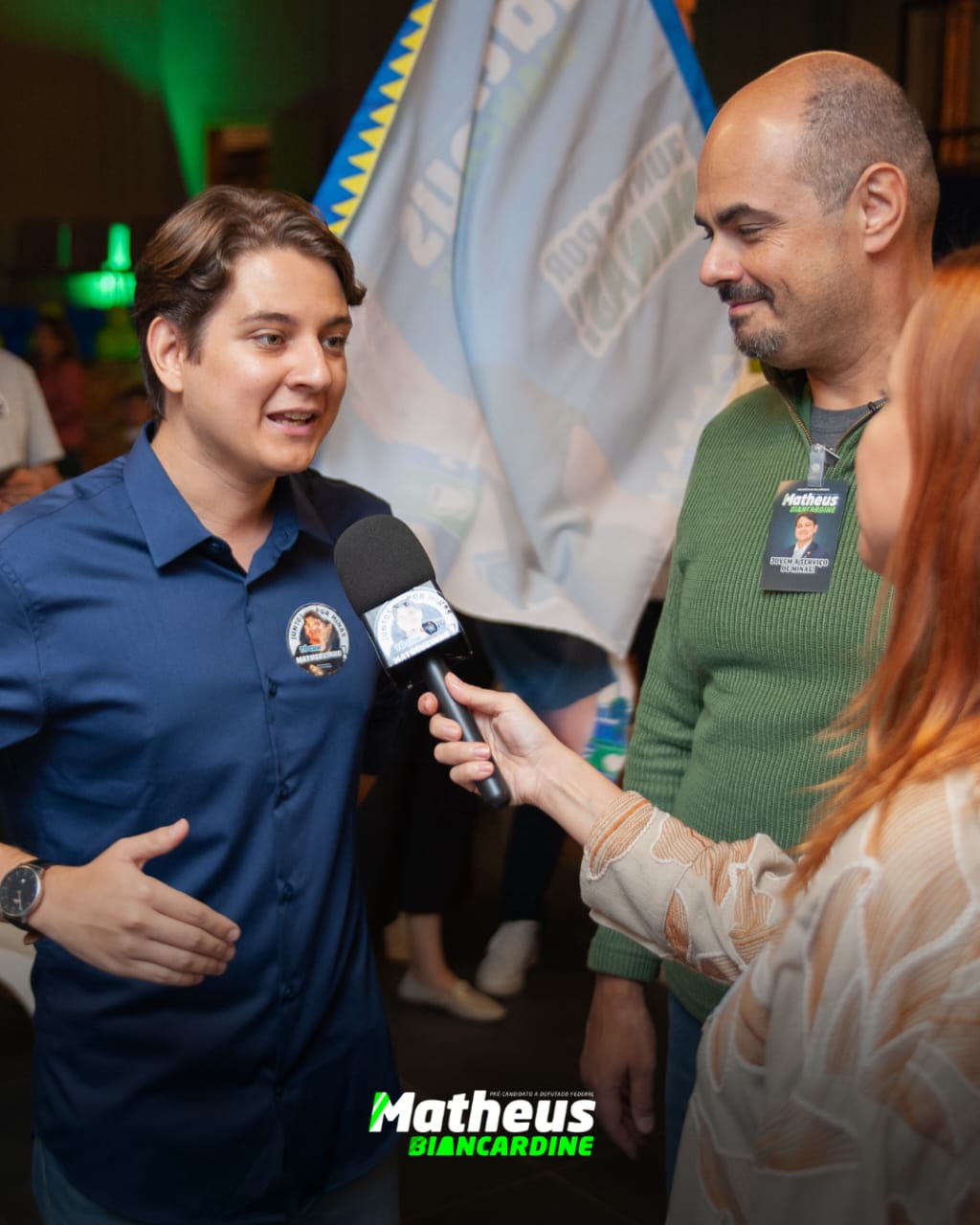 Matheus Biancardine concedendo entrevista com bandeiras da campanha ao fundo